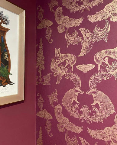 Burgundy and gold woodland wallpaper used as a dramatic feature wall in a warm, elegant interior